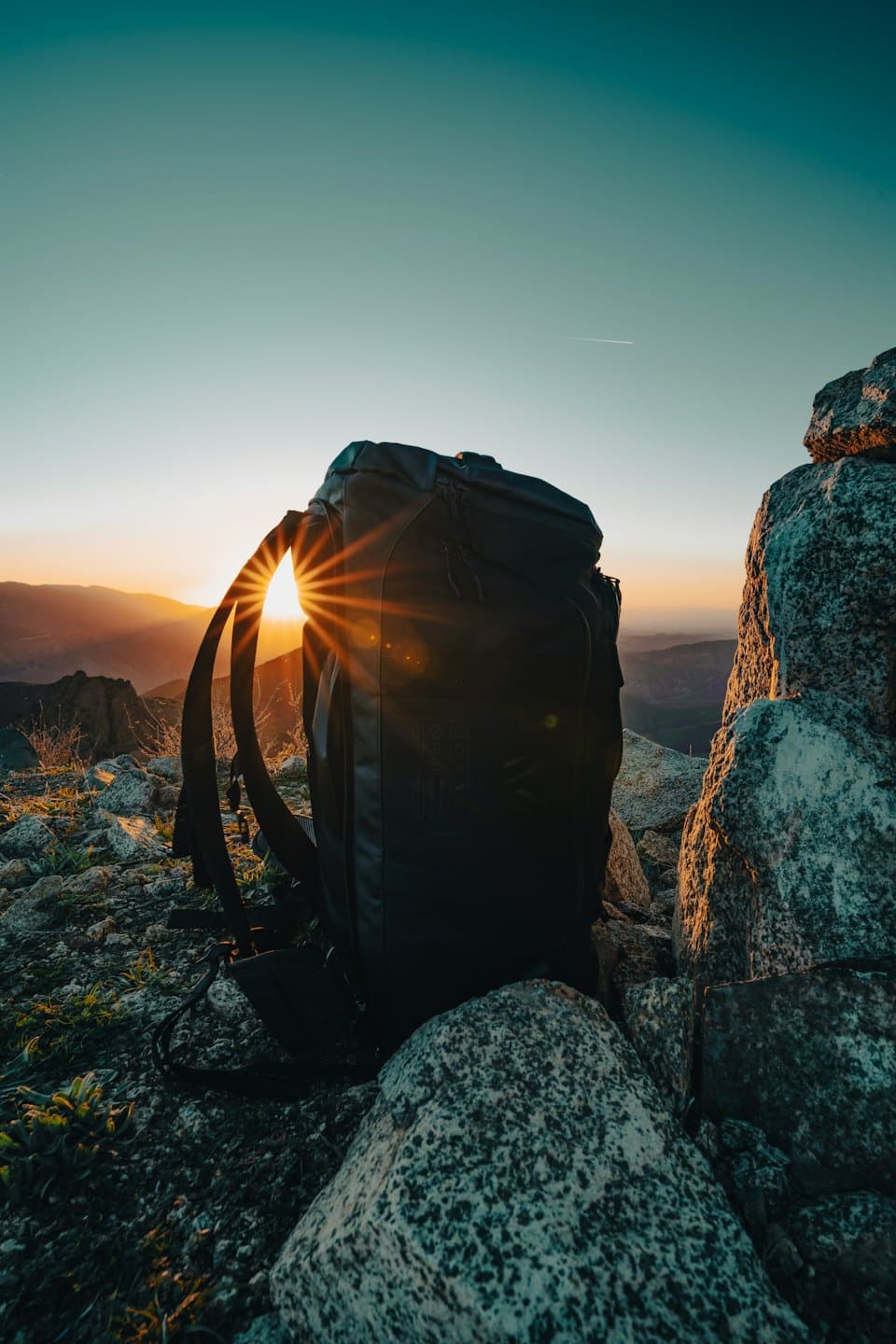 Black backpack rests on a rocky mountain summit at sunset.