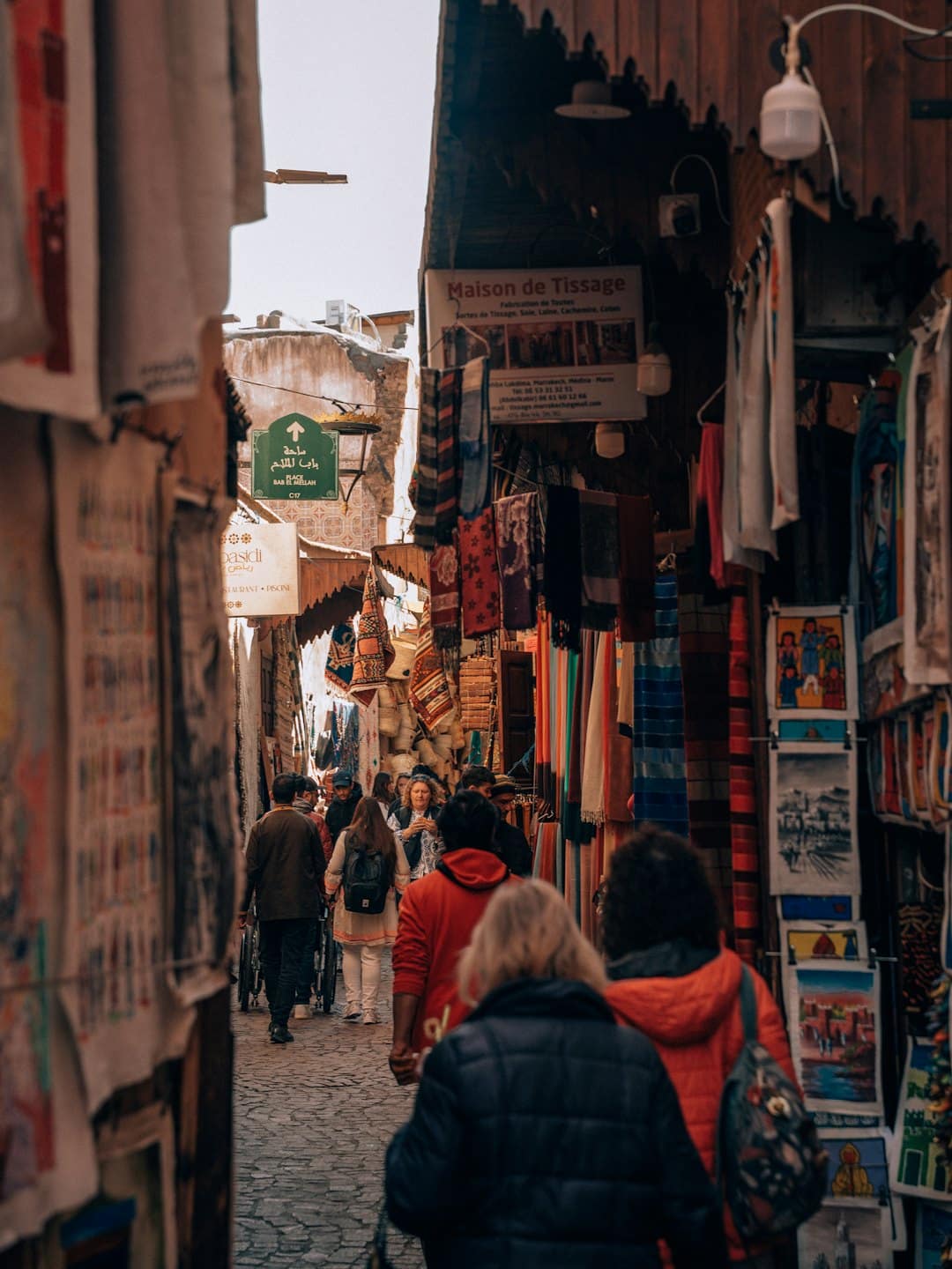 Shoppers walk through a bustling market street filled with textile stalls.